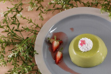 Elegant matcha panna cotta, a vibrant green dessert, topped with whipped cream and a delicate flower, served on a modern plate with fresh strawberry slices