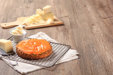 A delicious, peach cake sits on a cooling rack with grated and block cheese, and butter, on a rustic wooden background.