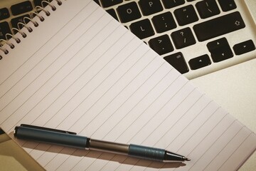 Open spiral-bound notebook with ballpoint pen is resting across laptop keyboard in flat design