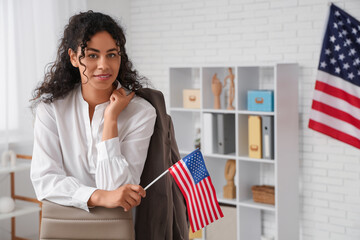 Beautiful young happy African-American businesswoman with USA flags in office