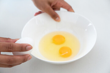 Photograph of a Latina woman's hands breaking eggs into a white bowl