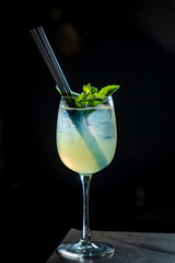 A vibrant cocktail with mint garnish and ice sits elegantly on a dark surface