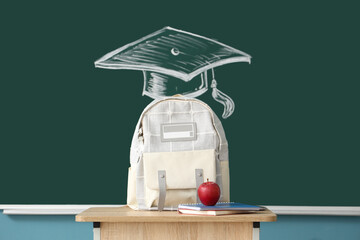 Backpack with apple on desk near blackboard in classroom