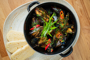 A pot of mussels with herbs and chili sits next to fresh bread, inviting a taste
