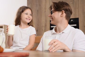 Little girl and her father with glasses of milk in kitchen