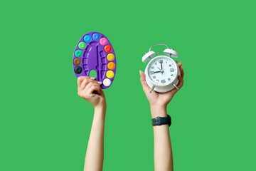 Female hands with palette and alarm clock on green background