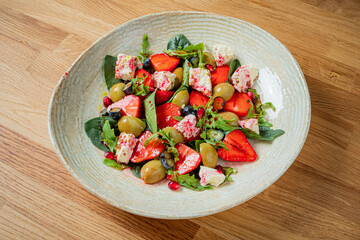 Enjoying a vibrant salad featuring strawberries, olives, feta, and greens served in a rustic bowl