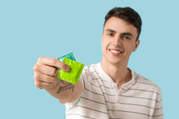 Young man showing condom on blue background, closeup