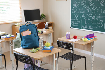 Apple with book, water bottle and backpack on desk in empty classroom