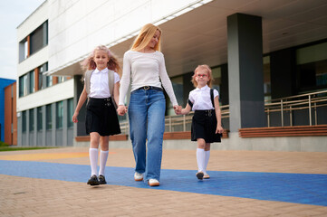 Fototapeta premium mother walking daughters to school entrance, hand in hand, showing family bond and education in modern urban setting during bright, sunny morning