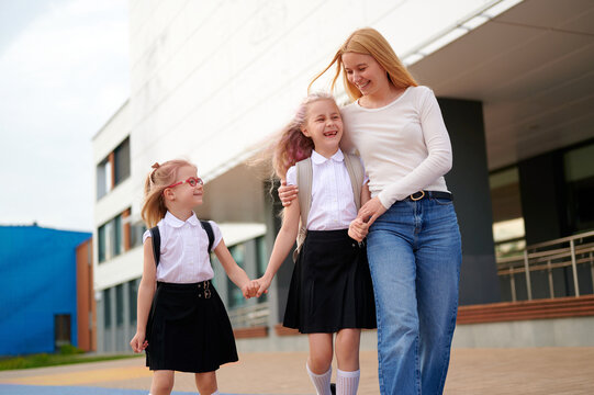 mother walks daughters to school, sharing joyful moments, holding hands. girls in uniforms with backpacks embrace educational adventure. happy family lifestyle, morning routine outdoors
