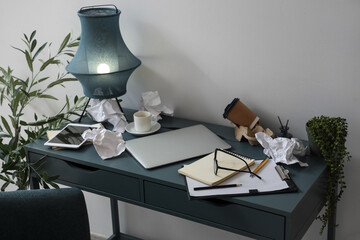 Messy workplace with modern laptop, lamp and papers in light office