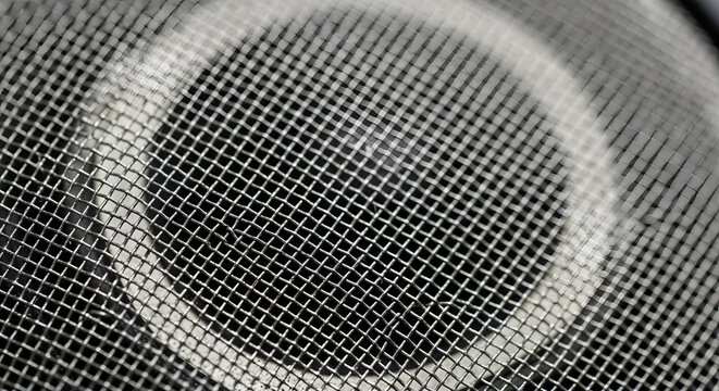 Macro photograph of a metal mesh speaker grill showing a circular pattern and texture