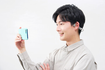 骨伝導イヤホンを付けてスマホを見る男性　20代　白背景