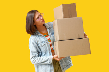 Beautiful young worried woman with parcels on yellow background