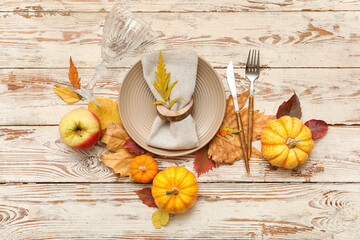 Beautiful table setting with fresh pumpkins, apple and autumn leaves on white wooden background