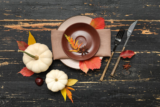 Beautiful table setting with fresh pumpkins, star anise, chestnut and autumn leaves on black wooden background