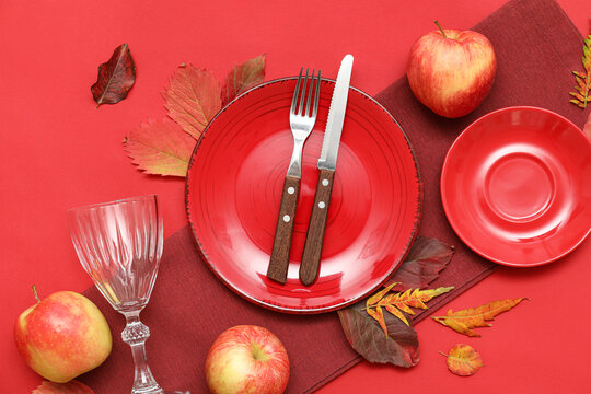Beautiful table setting with fresh apples and autumn leaves on red background