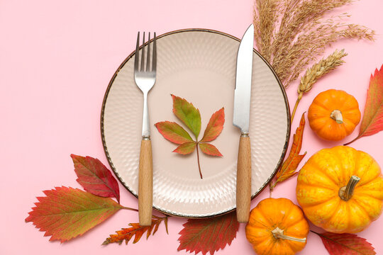 Beautiful table setting with fresh pumpkins, wheat and autumn leaves on pink background