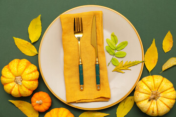 Beautiful table setting with fresh pumpkins and autumn leaves on green background