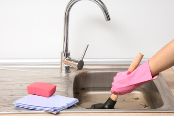 Woman cleaning clogged sink with plunger in kitchen