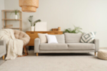 Blurred view of stylish living room with cozy armchair, grey sofa and wicker lamp