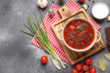 Bowl of tasty Ukrainian borscht and ingredients on dark background