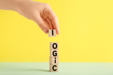 Female hand and cubes with word LOGIC on table against yellow background