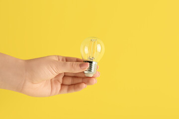 Female hand with light bulb on yellow background. Logic concept