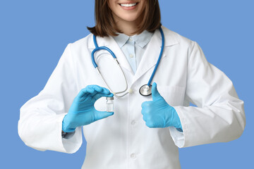 Happy female cardiologist with stethoscope and ampule showing thumb-up gesture on blue background,...