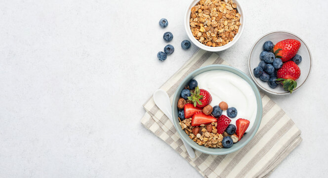 Yogurt with granola and berries in bowl on grey concrete background, table top view with copy space