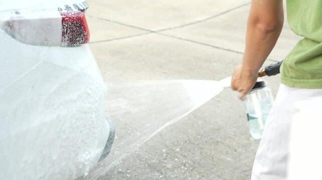 A middle-aged Asian man carefully washes his car using water and foam. Each step from high-pressure rinsing to scrubbing and drying ensures the vehicle is spotless, well-maintained, and presentable