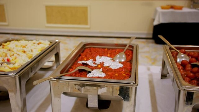 Stainless steel food trays with Indian desserts, chopped fruits and creamy sauce, gajar ka halwa or carrot pudding topped with sliced nuts, gulab jamun in syrup.