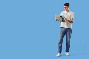 Handsome young man reading fashion magazine on blue background