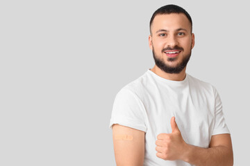 Young man with applied medical patch showing thumb-up on light background. Immunization concept