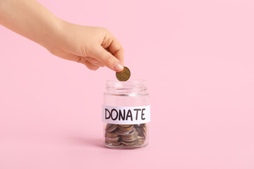 Hand putting money into jar on pink background. Donation concept