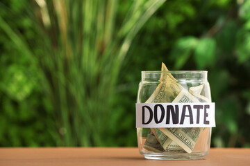 Jar with word DONATE and money on table outdoors
