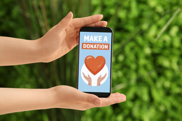 Hands holding mobile phone with open page of donation website outdoors