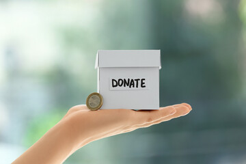 Hand holding box for donation and coin on blurred background