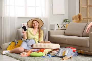 Young pregnant woman with passport, clothes, travelling accessories and full suitcase at home