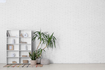 Shelving unit with decor and houseplants near white brick wall