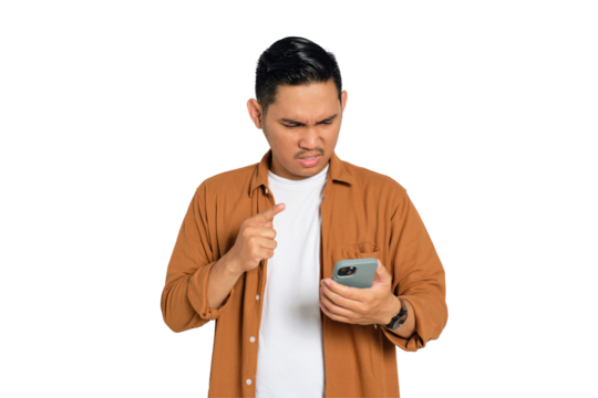 Angry young Asian man in casual shirt pointing with finger at his smartphone isolated on transparent background
