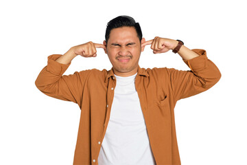 Irritated young Asian man in casual shirt plugging ears with fingers, disturbed by loud noise...