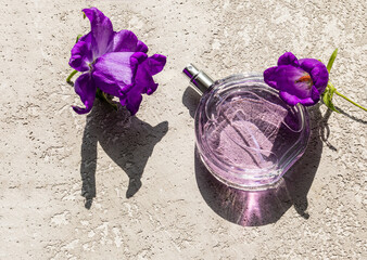 bottle of women's perfume with floral fragrance on a grey cement background with bright flowers. the sunlight of summer. A blank bottle mockup
