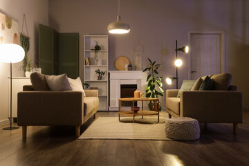 Interior of stylish living room with grey sofas, coffee table, fireplace and glowing lamps at...
