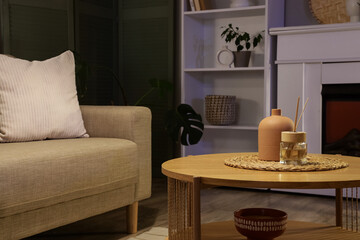 Interior of stylish living room with grey sofa, coffee table, fireplace and glowing lamps at evening