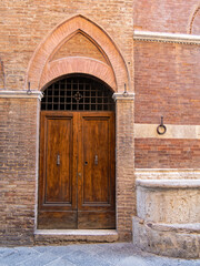 Elegant wooden door within a carved stone archway. The intricate details and textures highlight the region’s architectural charm. Travel to in Siena, Tuscany, Italy.