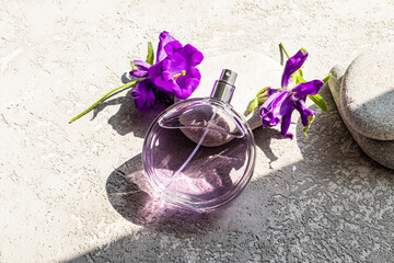A round bottle perfume was leaning on a gray stone among the purple flowers of the bell. Blank Bottle Mockup. Presentation of a floral fragrance.
