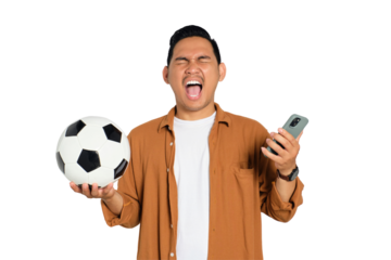 Excited young Asian man in casual shirt holding soccer ball and smartphone, shouting yes, celebrating victory isolated on transparent background