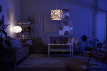 Interior of stylish living room with cozy sofas, coffee table and glowing lamps at night